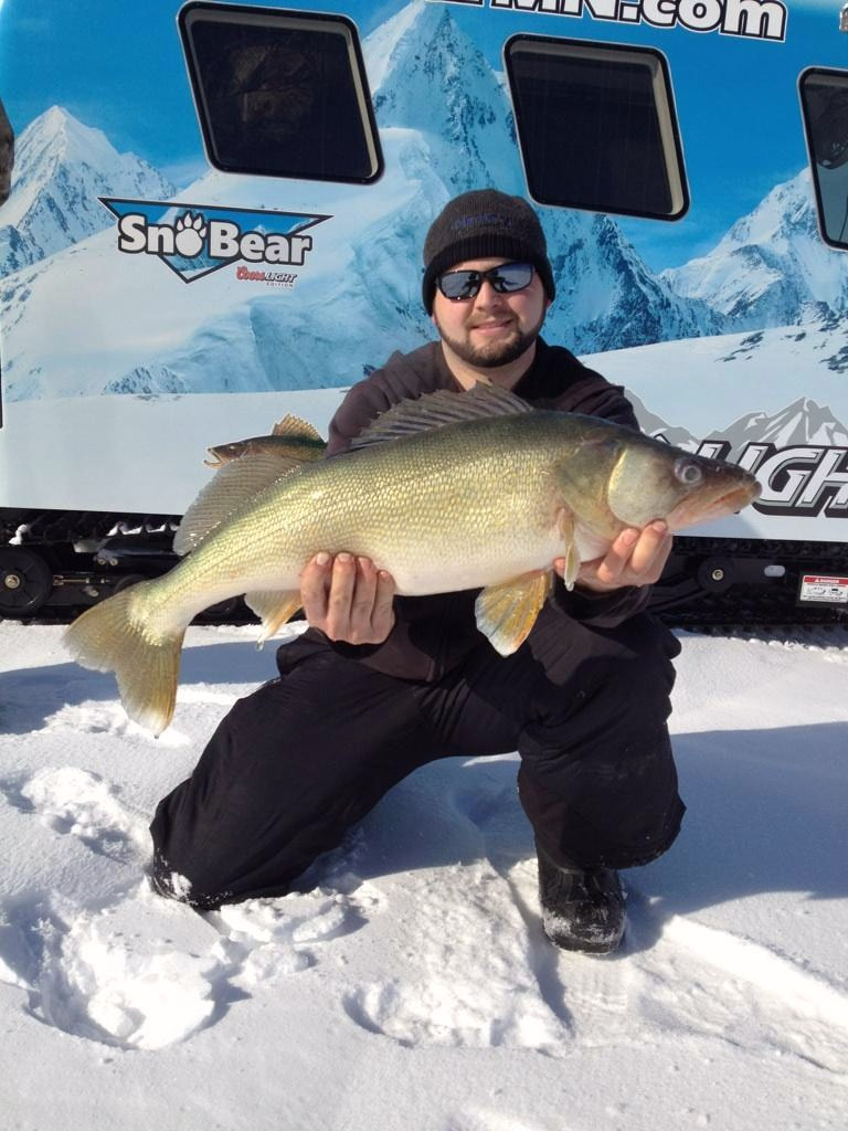 Man on snow and ice covered lake holding greenback walleye caught while ice fishing in Canada.